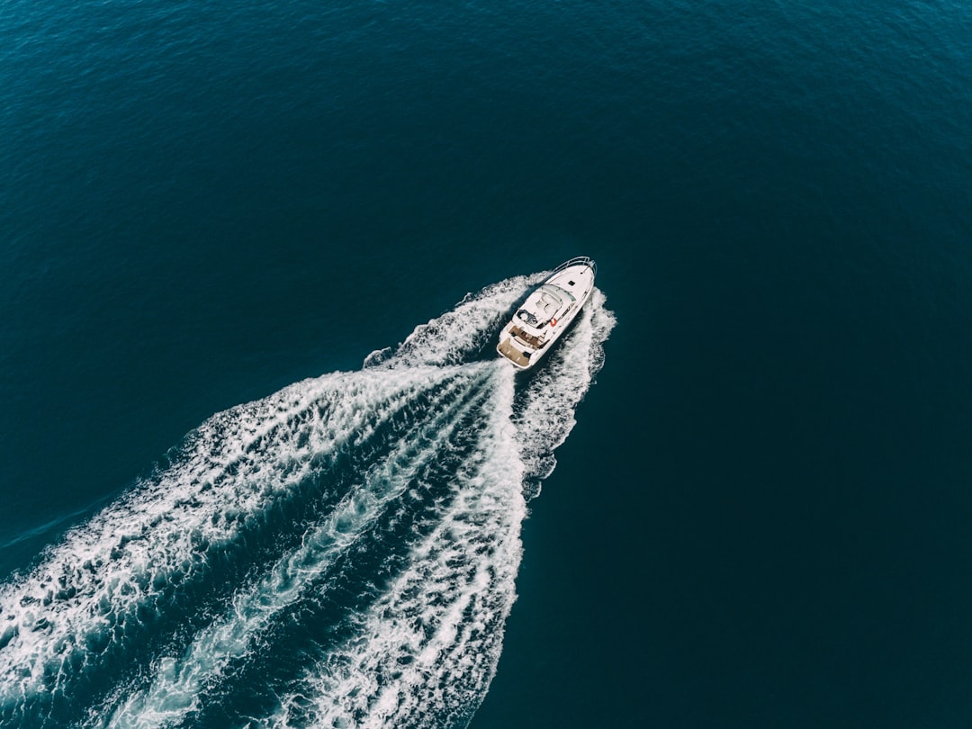 Aerial view of a white yacht cruising through deep blue waters, creating waves behind it.