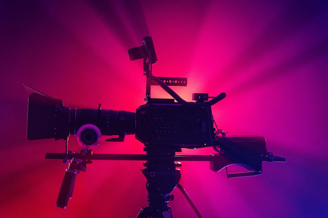 A professional camera on a tripod with colorful lighting in the background.